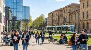 Étudiants marchant sur le campus Tréfilerie à Saint-Étienne avec un tramway en arrière-plan.