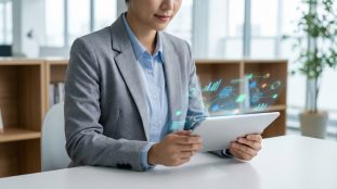 Femme d'affaires en blazer gris utilisant une tablette avec des projections holographiques de graphiques et réseaux de données, en milieu de bureau.
